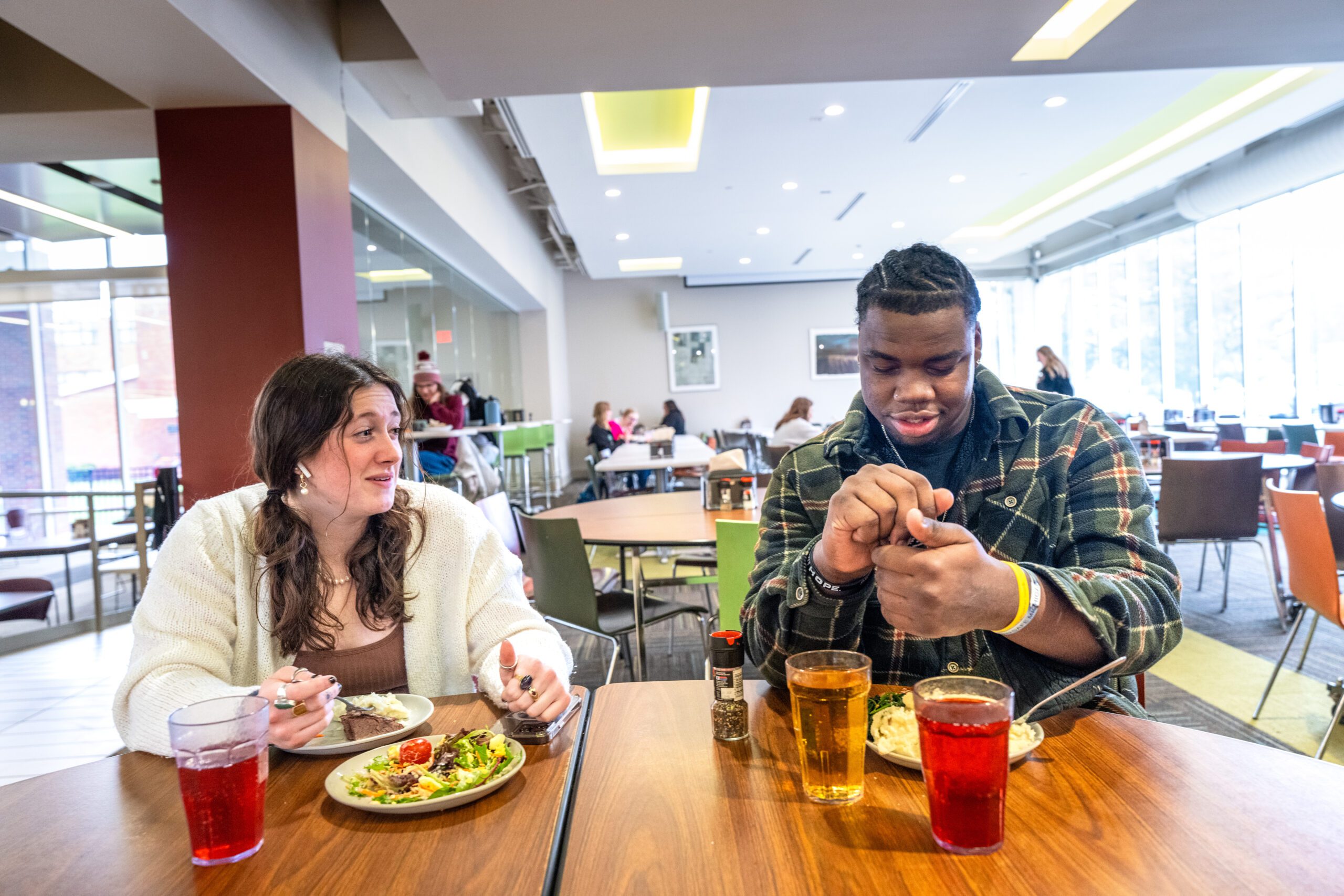 Two students eating and talking while seated at a table at Hamilton Commons while salting their food.