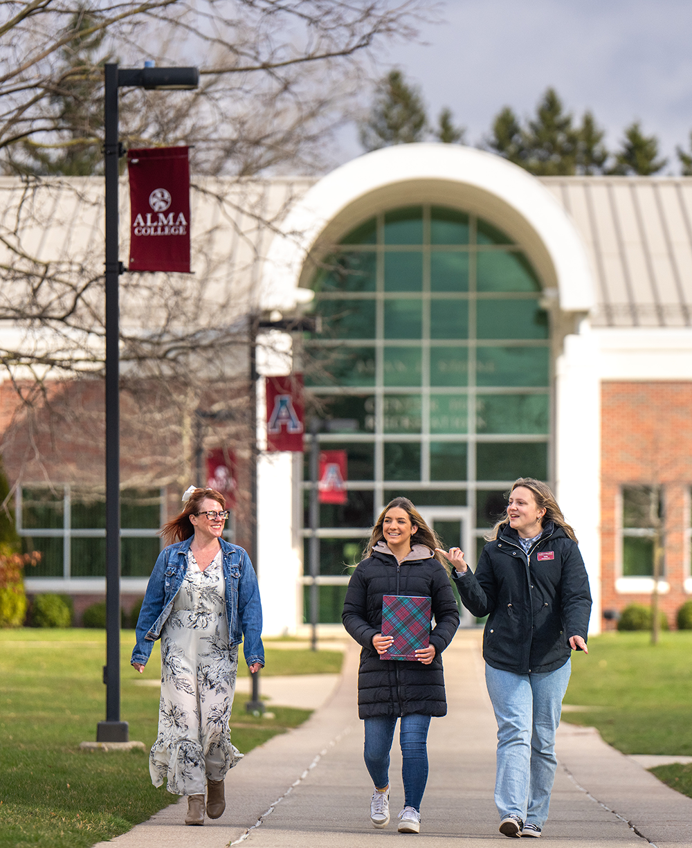 A student and their parent on a tour on campus walking in front of the Stone Recreation Center as the tour guide points and describe something off in the distance.