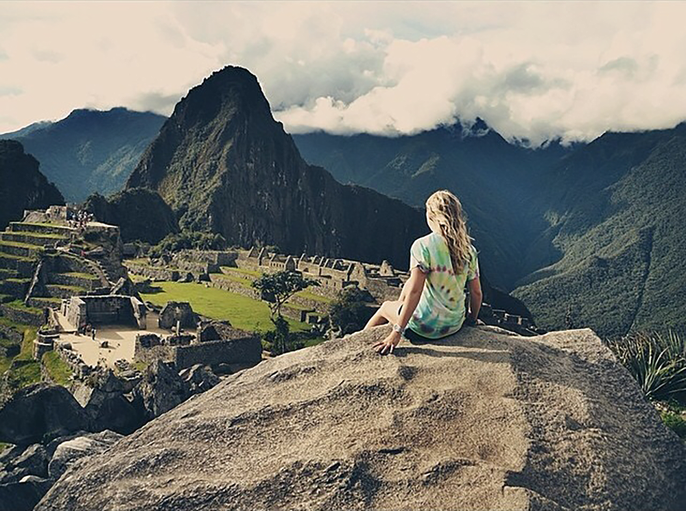 A student sitting on an overlook looking at ruins in Peru.