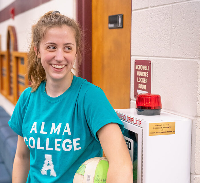 Alma College student holding a volleyball under her arm while stanind in from of the Women's Locker Room inside the Stone Recreation Center on the campus of Alma College.