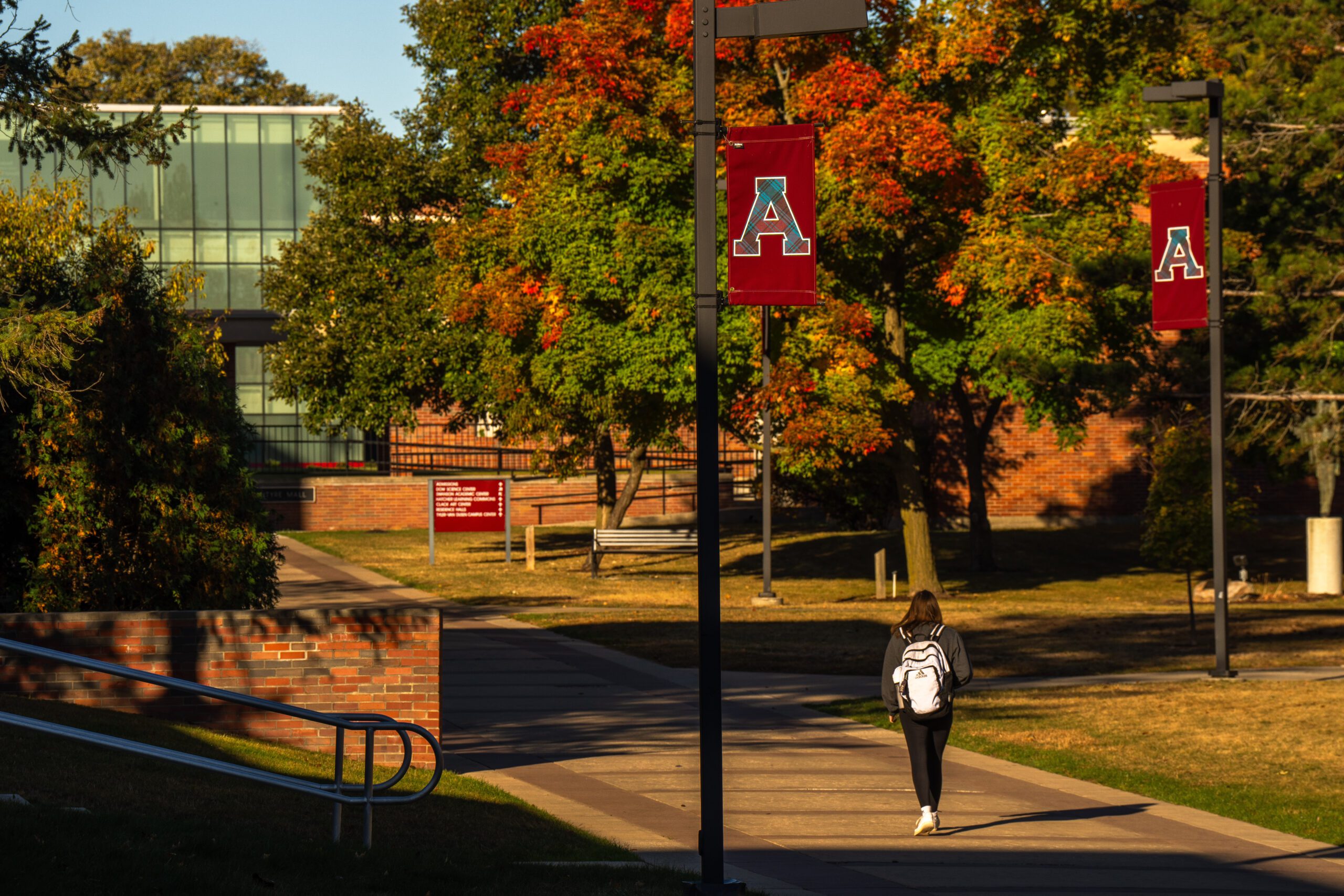 Student wearing a white backpack walking down a sidewalk on a beautiful fall day on the campus of Alma College.