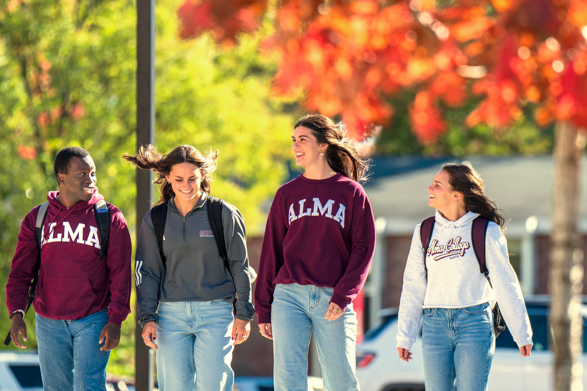 Group of four students walking down the sidewalk on a sunny fall day talking and smiling.