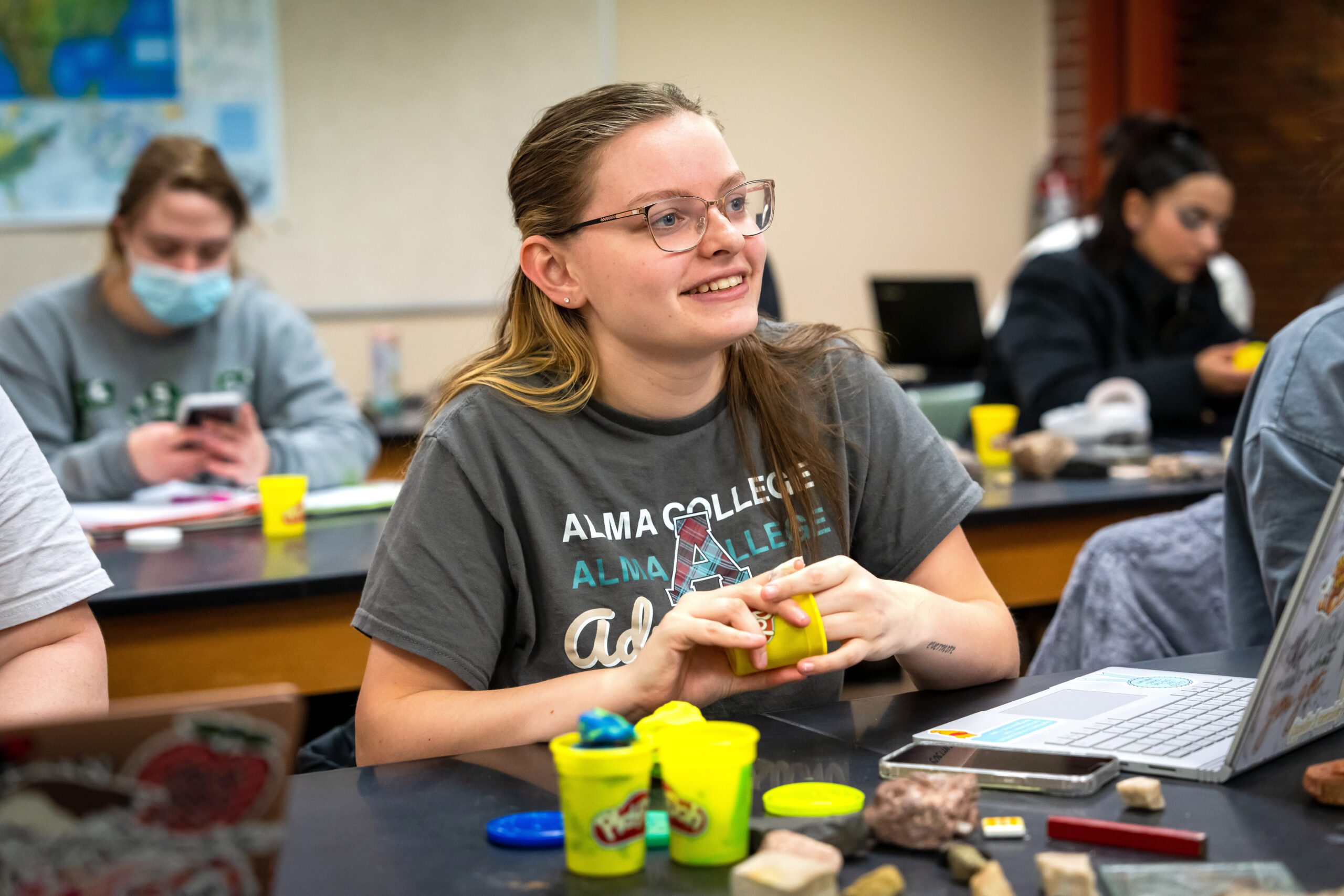 A college student attentively listens to their professor while making a geological model with Play-Doh.