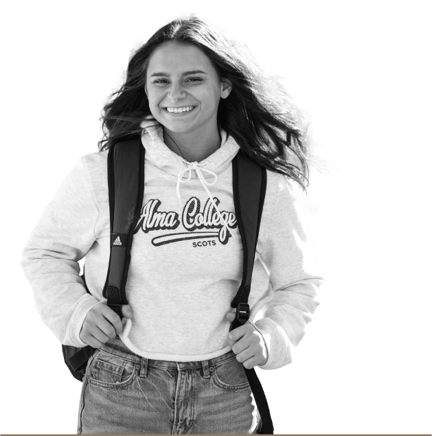 Female student smiling and looking at the camera, wearing an Alma College sweatshirt and backpack